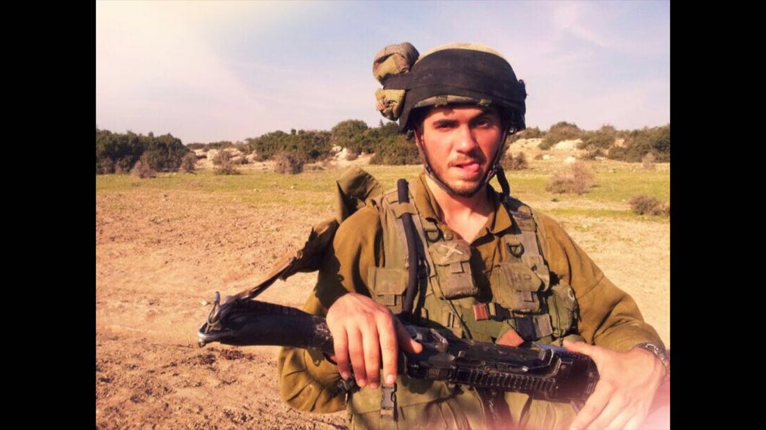 Daniel Reichenbach in Israel Defense Forces uniform and helmet holding a machine gun during a field training exercise