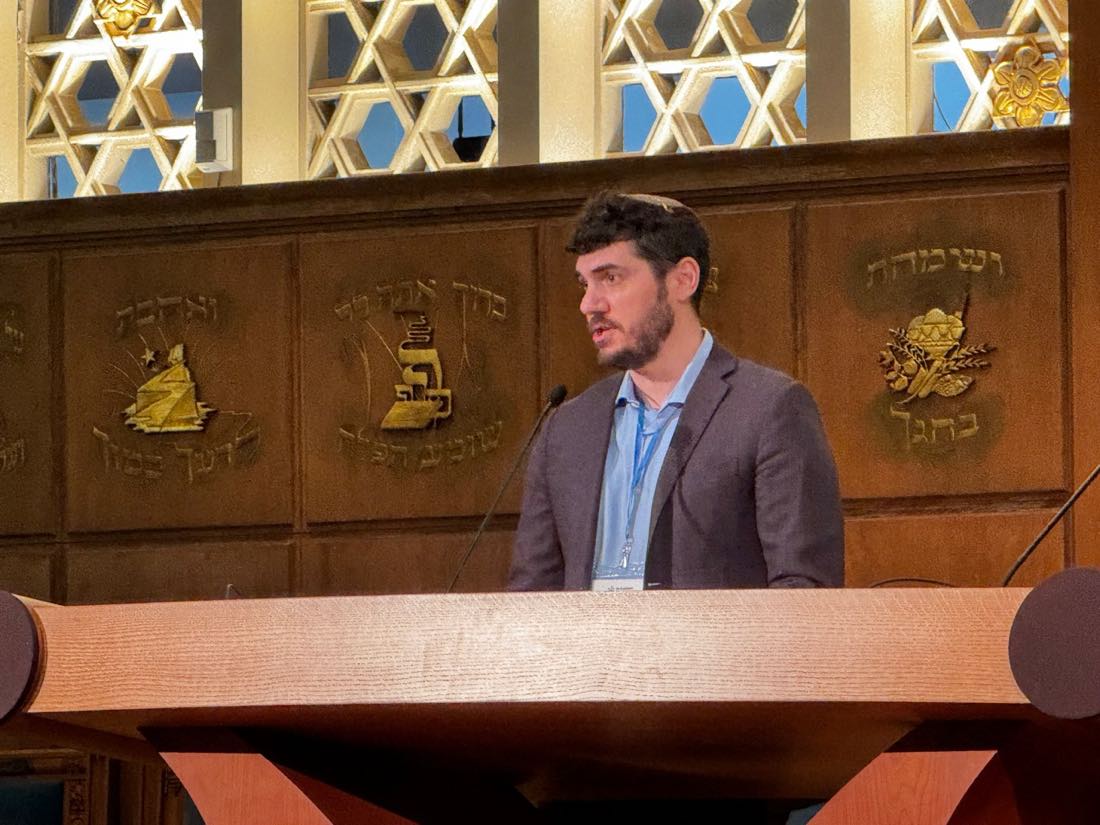 Daniel Reichenbach speaking from a synagogue lectern while introducing Rabbi Ami Hirsch as a keynote speaker at Recharging Reform Judaism