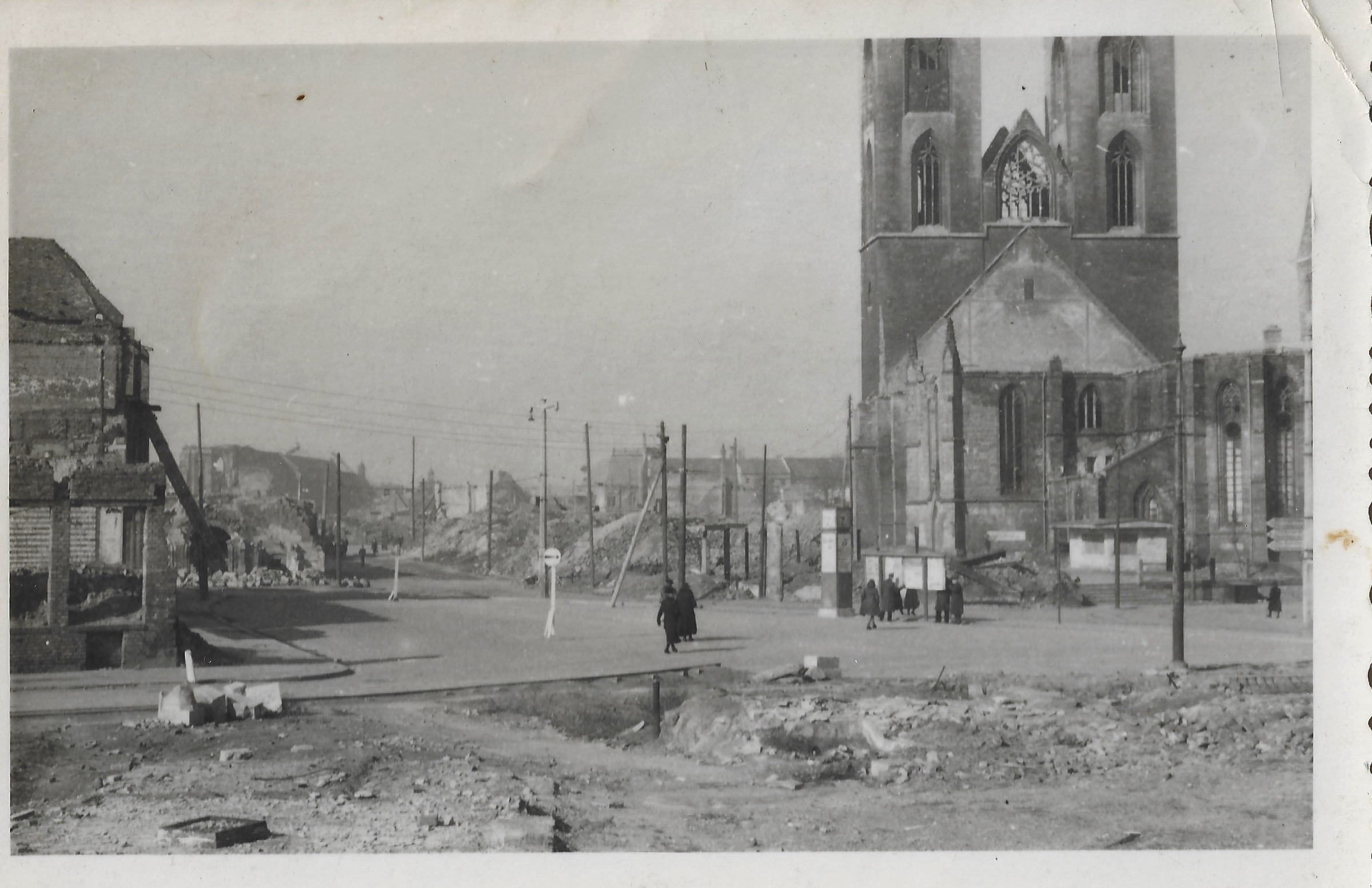 Black-and-white family-held photograph of Halberstadt’s ruined center after the 1945 bombing, with rubble, pedestrians and the damaged twin-towered Martinikirche at right
